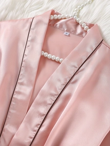 Détail du col d'un peignoir en satin rose avec étiquette S sur fond de fausse fourrure