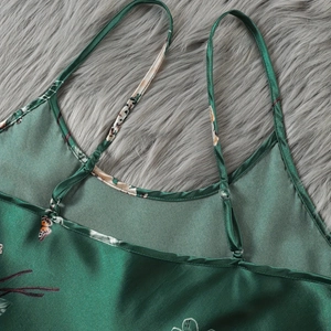 Pigiama in raso verde con stampe floreali e spalline regolabili su superficie morbida