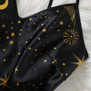 Schwarzes Satin-Top mit goldenen Sonnen- und Mondmotiven auf weißem Fellhintergrund