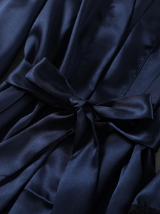 Detail of a dark blue satin robe showing the silky fabric texture and a tied waist bow