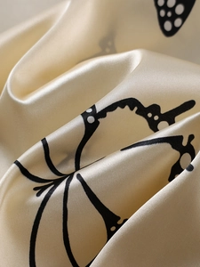 Detailed close-up of champagne satin fabric with black butterfly prints and silk texture