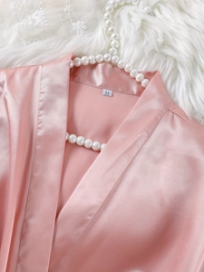 Détail du col d'un peignoir en satin rose avec étiquette sur texture peluche