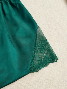 Dettaglio dell'orlo di un pigiama in raso verde scuro con pizzo elegante e trama in seta