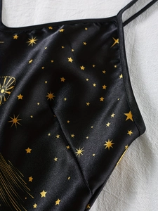 Vue détaillée du tissu satiné noir avec imprimé étoiles dorées et finitions dentelle
