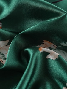 Macro del tessuto del pigiama in raso verde scuro con stampa botanica arancione