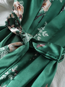 Dettaglio della vestaglia in raso verde scuro a fiori con cintura e trama setosa