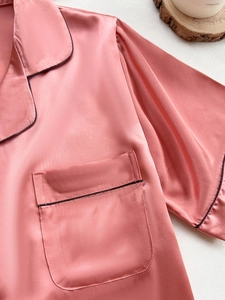 Detail of coral pink satin pajama top featuring black piping and classic lapel collar