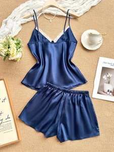 Flat lay of navy blue silk pajama set with white lace trim and V-neck top on woven mat