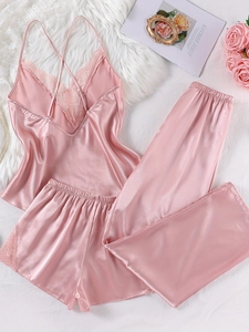 Flat lay of three-piece pink satin pajama set with delicate lace trim on white fur background