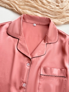 Close-up of pink satin pajama top with notch collar, black piping and pocket detail