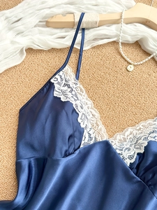 Detailed view of dark blue satin camisole with white lace embroidery on a wooden hanger