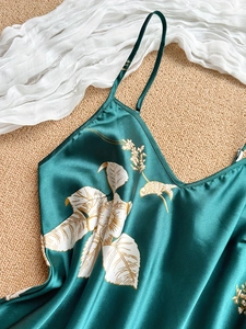 Detailed flat lay of dark green satin sleepwear with elegant white leaf patterns and gold outlines