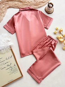 Detail of pink satin pajama set with short-sleeved top and pants featuring dark piping