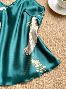 Detailed close-up of dark green silk satin pajamas with elegant crane and floral prints