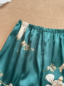 Detail of emerald green satin pajamas with elastic waist and white crane floral prints