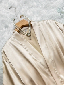 Flat lay of champagne silk satin V-neck robe with pearl necklace on a white plush rug
