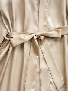 Detailed close-up of champagne silk satin robe featuring a tied waist belt on soft carpet