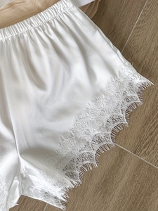 Détail de short de pyjama en soie glacée blanche avec bordure en dentelle sur fond bois