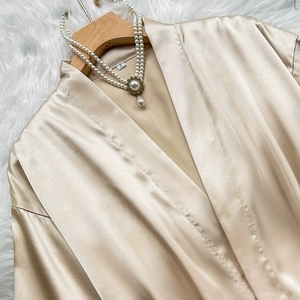 Champagne silk satin robe with kimono collar on wooden hanger against white fur background
