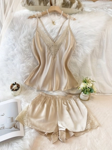 Detailansicht von champagnerfarbenem Seidenpyjama-Set mit Spitze auf weißem Teppich