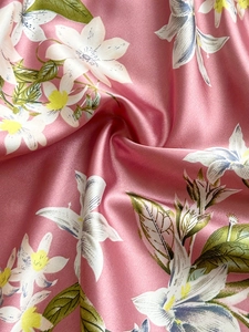 Close-up of pink silk fabric with floral lily print showing smooth satin texture and shine