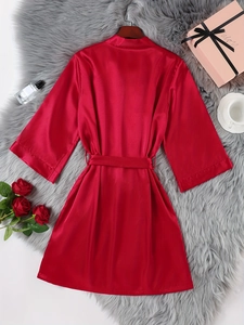 Detailed flat lay of a red satin bathrobe with matching belt on a luxury plush carpet