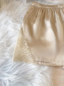 Detail von champagnerfarbenen Satin-Schlafshorts mit Spitze auf weichem Plüschgrund
