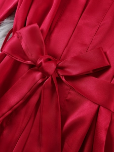 Detail of red satin robe waist with a large bow tie and elegant vertical pleated texture
