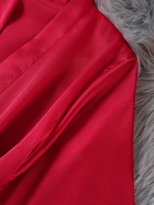 Close-up of deep red satin robe fabric texture showing smooth silk shine and fine stitching