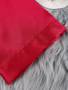 Detail of red satin robe hem with delicate stitching on a soft plush grey surface