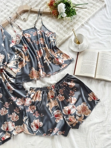 Dreiteiliges Satin-Pyjama-Set mit Blumenmuster und Robe auf einem gemütlichen weißen Bett