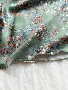 Close-up of sage green floral satin dress featuring a delicate wavy lettuce edge hemline