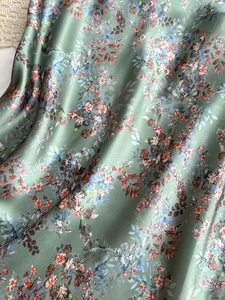 Detailed macro view of sage green floral satin fabric with smooth silk-like texture