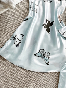 Détail du tissu en satin bleu clair pour pyjama avec imprimé papillon et texture soyeuse