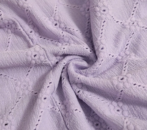 Dettaglio del tessuto ricamato lavanda con trama plissettata e motivi traforati eleganti