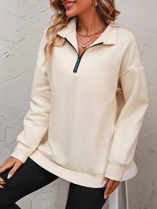Close-up of cream half-zip sweatshirt with black zipper detail and ribbed cuffs