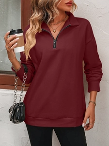Detail of burgundy half-zip sweatshirt with ribbed cuffs and fleece texture in city setting