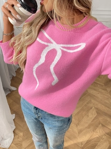 Detailed view of a pink knit sweater featuring a white bow jacquard pattern on a model