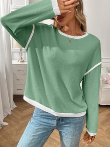 Detail of the light green knit sweater showing the white contrast ribbed neckline and hem