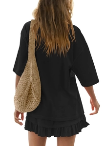 Rear view of black oversize t-shirt and pleated mini skirt paired with a beige straw bag