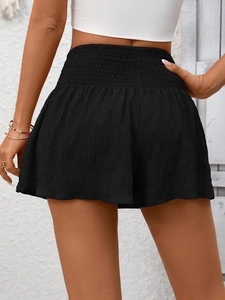 Detail of high waisted black smocked shorts with elastic waist and textured fabric