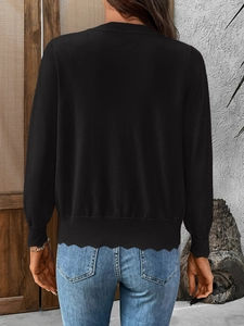 Detail of black knit cardigan featuring a scalloped hemline and ribbed sleeve cuffs