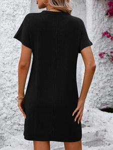 Detail of black ribbed knit short sleeve dress back view against a white wall with pink flowers