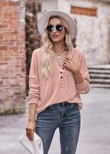 Detail eines rosa Waffelstrick-Kapuzenpullovers mit V-Ausschnitt und Knöpfen am Model