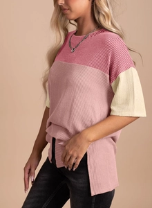 Detail of color-block ribbed knit top with side slit hem and soft pink texture