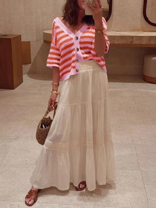 Detail view of pink and orange striped V-neck knit cardigan paired with a white lace skirt