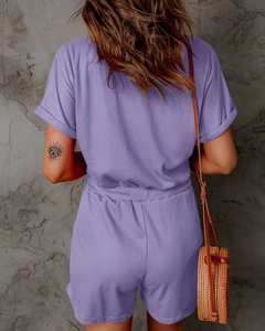 Rear view of purple ribbed knit romper with cuffed sleeves and woven straw bag detail