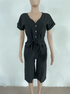 Détail d'une combinaison noire avec col en V, boutons et ceinture nouée à la taille