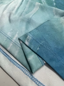 Macro detail of geometric tie-dye fabric showing double-needle hem stitching and texture