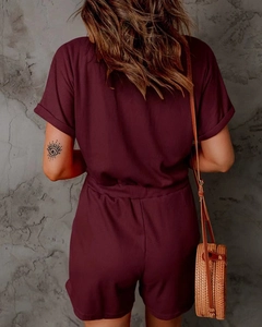 Back view of a burgundy ribbed knit jumpsuit with cuffed sleeves and a round straw bag